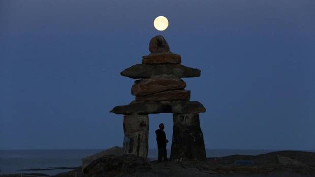 A man looks at a giant inukshuk as the moon rises above it in Rankin Inlet, Nunavut in this file photo from August 21, 2013.
